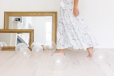 Abby Manawes in a white and black dress kicking clear balloons on the floor