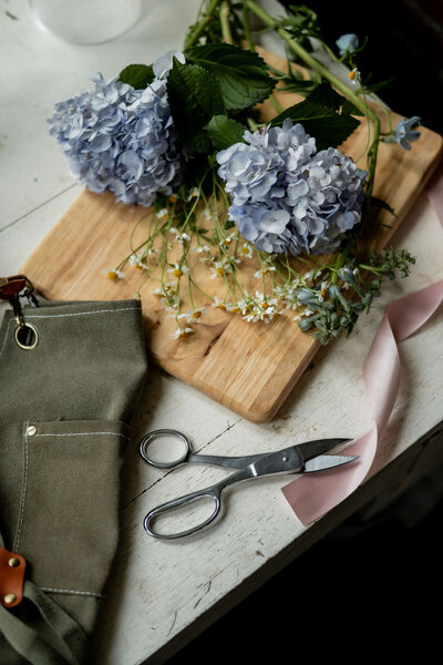 A flat lay of floral tools, flowers, and ribbons on a table