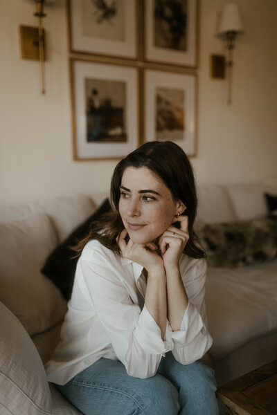 Woman wearing white collared shirt sitting on a couch a leaning forward looking to her right