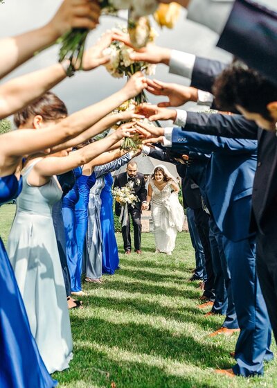 Wedding party holds up hands as bride and groom run under it