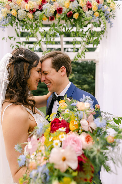Wedding Photographer, a bride and groom are nose to nose smiling, she has flowers in her hand