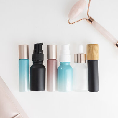 assortment of serum and dropper bottles in a variety of colors with pink jade roller above them