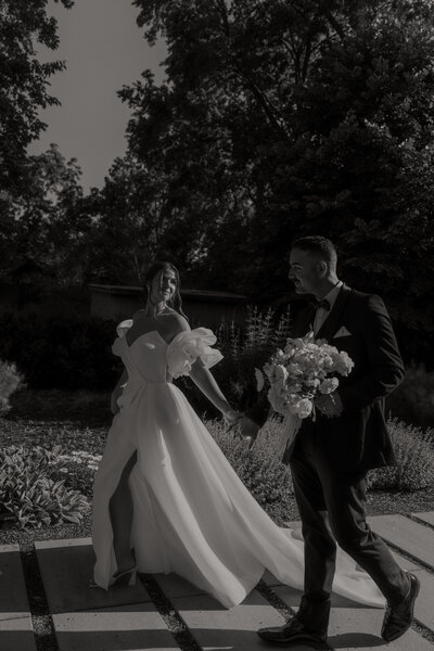 bride and groom walking hand in hand in harsh light black and white photo
