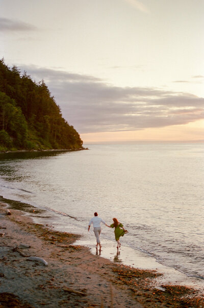 engaged couple running down a beach at sunset