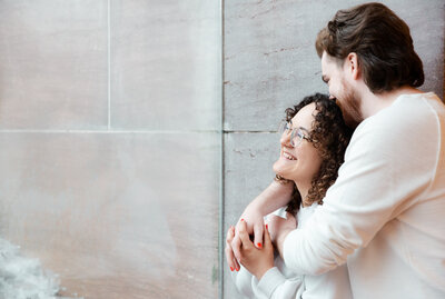 During their elopement, a bride with curly dark hair and glasses is embraced by her groom with dark hair and beard photographed by Caia Grace