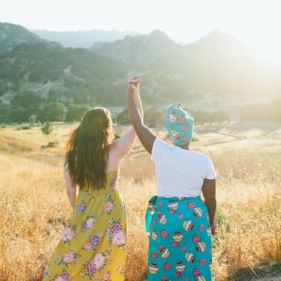 two women holding hands up standing in a golden field