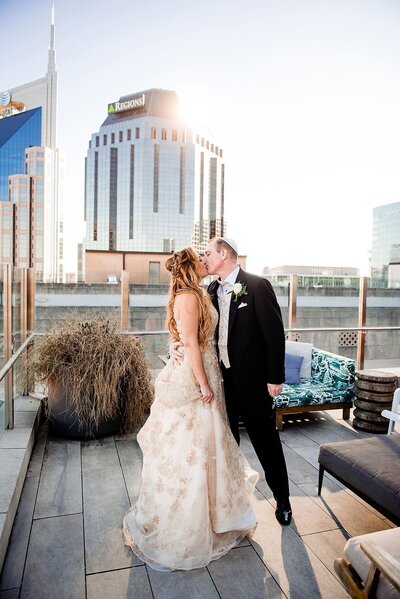 Bride and groom sharing a kiss on top of the Noelle hotel in Nashville with the skyline behind them