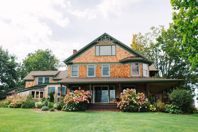 A brown cedar shake house with green trim and pink hydrangea bushes out front a