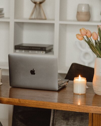 Calming workspace with a MacBook on a wooden table, lit candle, and vase of tulips for focused web design