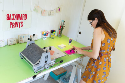 Woman in mustard dress creating handmade card on stamp press for showcasing product image on website.
