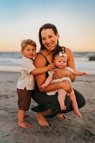 A woman holding a baby and a boy on a beach.