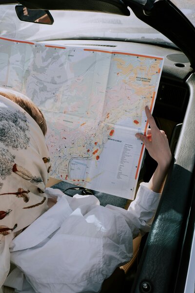Woman with a vintage headscarf holding up a map in the front seat of a car
