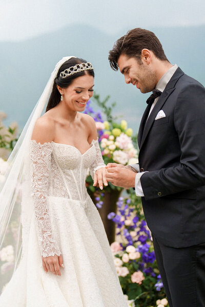 bride and groom smiling while groom places ring on bride's finer