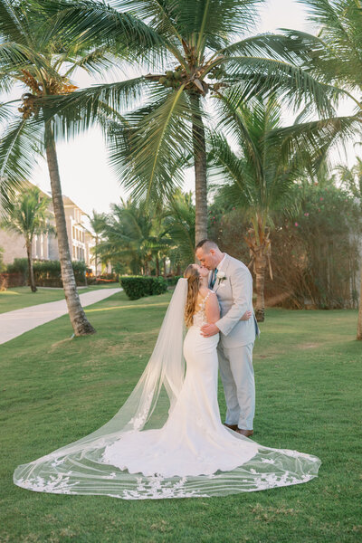 A couple kisses near some palm trees at their wedding in Punta Cana