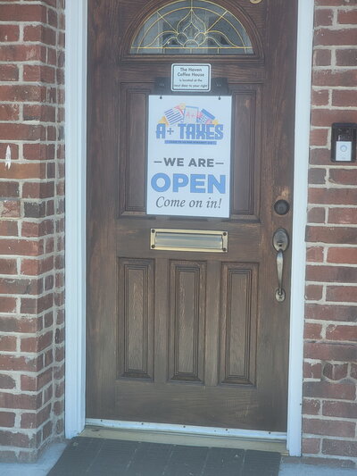 Front door of A+ Taxes office with a sign that reads "We are open, come on in," welcoming clients in Nephi, Utah