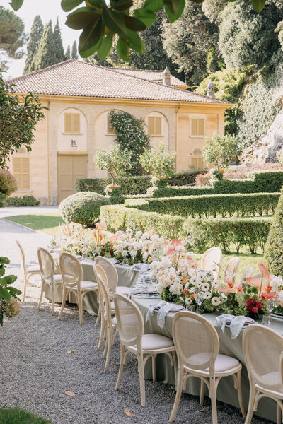 villa pizzo has a garden reception table in the gardens along lake como. the yellow villa is the perfect backdrop for the green, pink, and white flowers on the serpentine table. image by philadelphia wedding photographer emily wilkerson