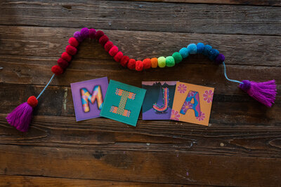 A piece of artistic brilliance showcased on a wooden table, adorned with a prominent brand word and surrounded by a burst of colorful pom-pom.