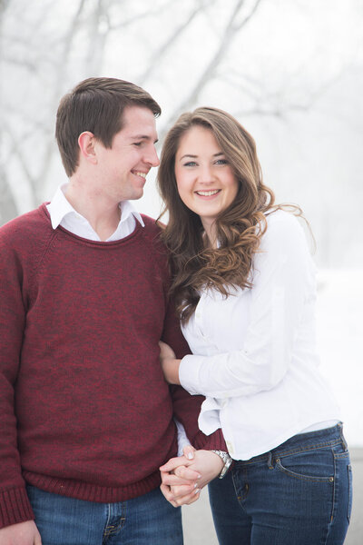 happy engaged couple snuggled together laughing in a foggy winter wonderland