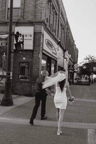 A couple walking across the sidewalk in Collingwood, Ontario during their elopement themed engagement shoot
