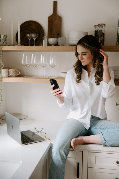 Website copywriter Erika Fitzgerald sitting on a kitchen counter looking at an iPhone