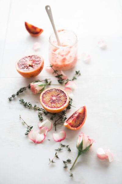 a cocktail glass with muddler sitting with blood orange and rosemary springs all around it on a white background for graphics creation socialfizz