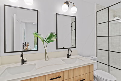 Contemporary bathroom featuring a white double vanity with black fixtures, wood cabinetry, dual mirrors, and a black-framed glass shower enclosure