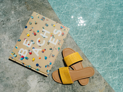 Book and yellow sandals laying on the edge of the pool