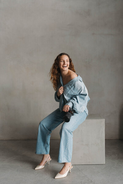 a woman sitting on a block laughing and holding a camera