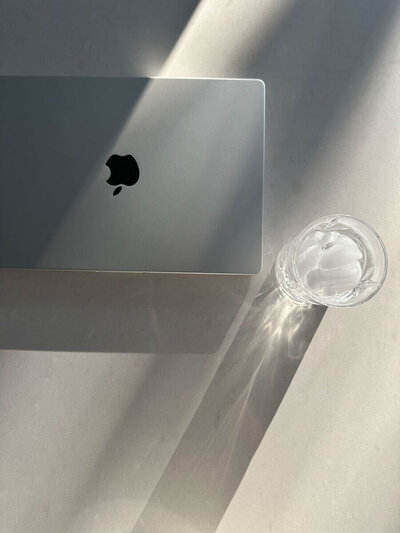 Macbook computer on a light colored table with a glass of water