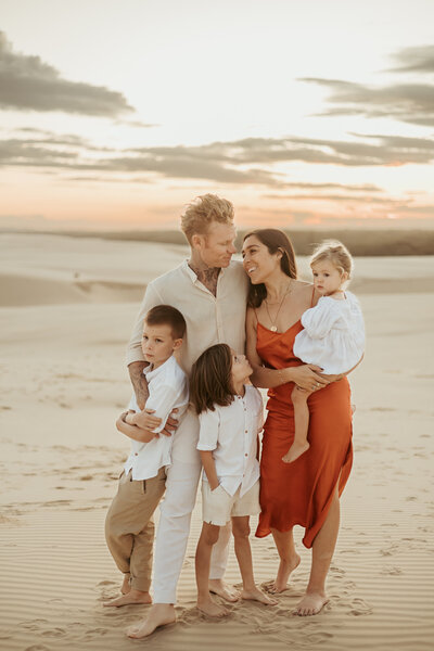 Beautiful family of five standing together cuddled up at the sand dunes.