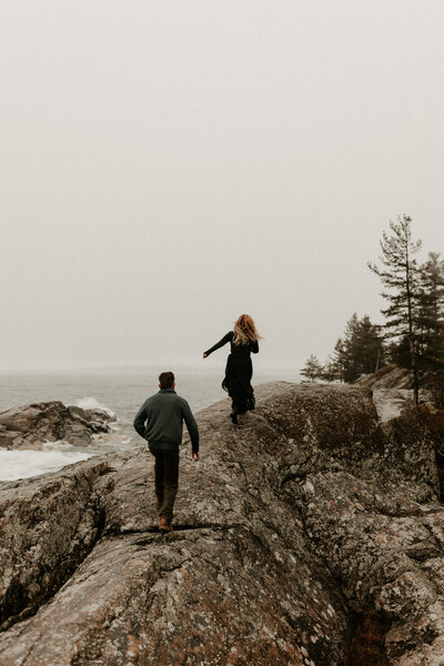 couple running up a rock at Wetmore Landing during engagement session in Upper Peninsula of Michigan