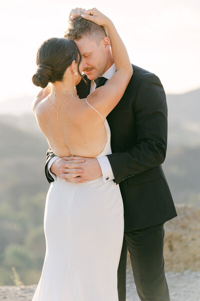 bride and groom romantic embrace during golden hour on top of the hill at cielo farms captured by malibu wedding photographer magnoli west
