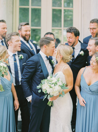 bride and groom kiss while their wedding party celebrates