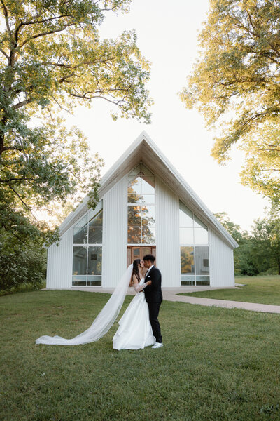 Classic wedding photo of bride and groom standing outside of their venue while embracing each other