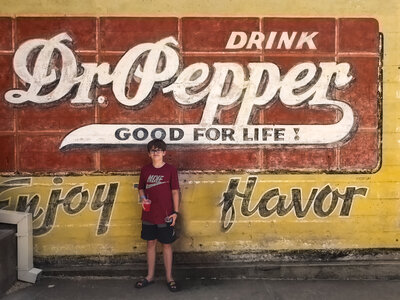 Kelly Loss's son stands in front of a Dr. Pepper sign