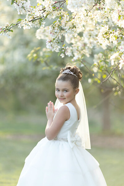 Young girl in her 1st Holy Communion dress & veil posing under a white flowering tree in a NJ park.