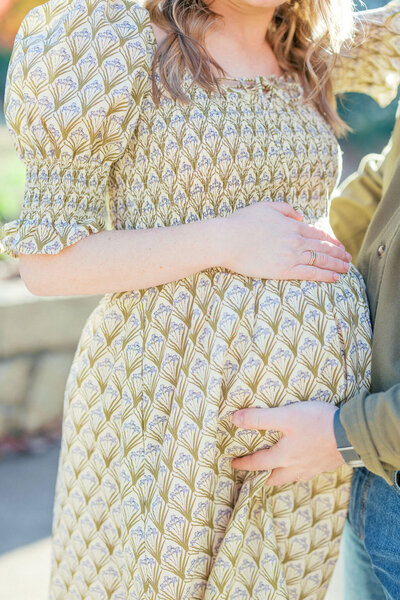 Woman in green patterned dress holds baby bump with husband