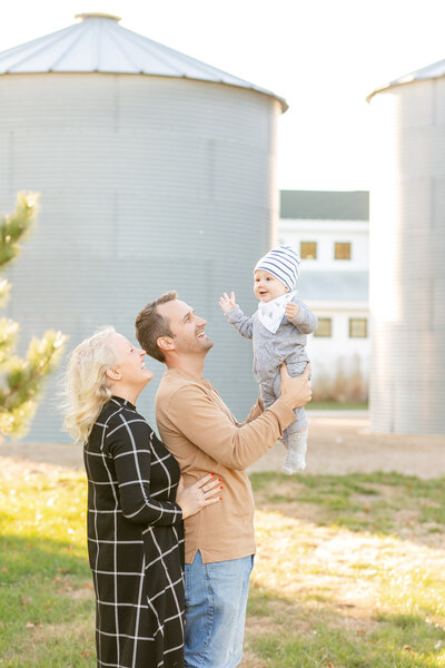A white couple throwing their baby in the air with silos in the background