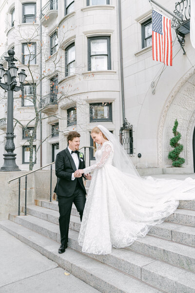 a man helping his bride down the front steps of the Harvard Club