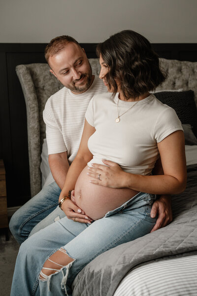 A couple sharing a quiet moment during their maternity session, sitting together on the bed in their Nottingham home. Captured in soft natural light to reflect the warmth and intimacy of expecting a baby.