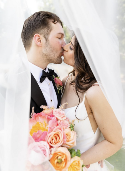 newlywed couple kissing while bride holds colorful bouquet