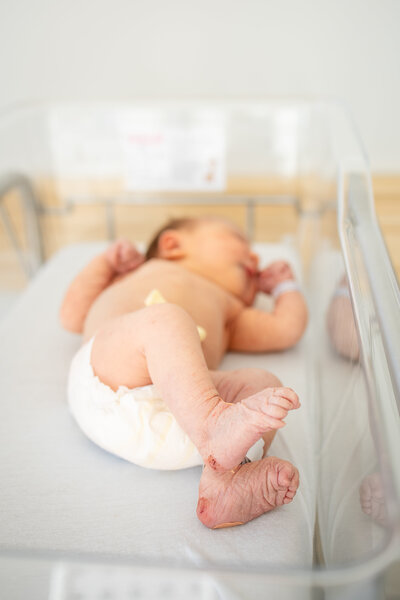 Newborn baby girl in diaper laying in bassinet