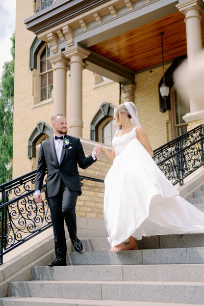 groom helping a bride walk down the steps