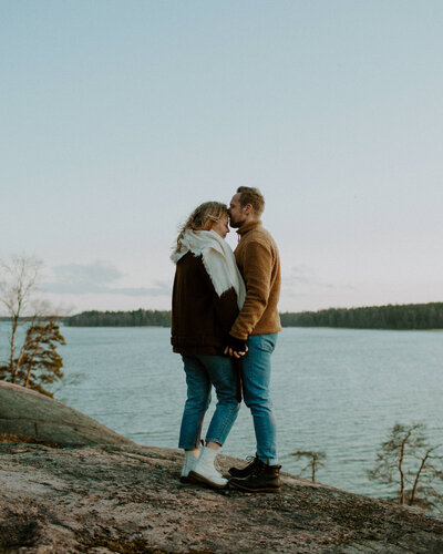 Kihlapari seisoo rantakalliolla vastakkain pidellen käsistä toisiaan ja päät vastakkain Kivenlahdessa Espoossa