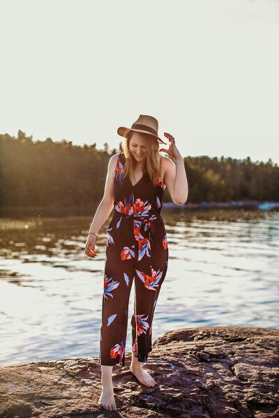 woman in floral jumpsuit and hat standing on rock
