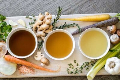 Two china cups of broth on board with vegetables