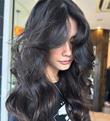 Brunette hair styled in voluminous waves with glossy highlights, captured in a modern hair studio.