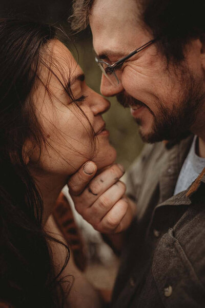 A dad lovingly holds his wife by the chin. Their eyes are closed and their noses are touching