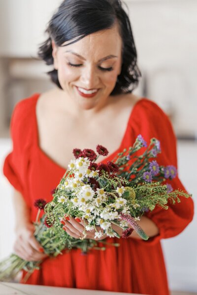 Nashville-Family-Photographer-Headshot-of-Dolly-DeLong-Photography-wearing-a-red-dress-and-smiling-at-wildflowers
