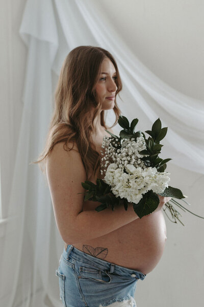 Pregnant woman holding flowers to her bare belly during a studio maternity session